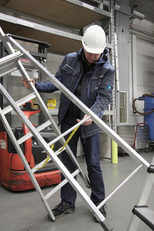 Arbeiter hält eine ZARGES Stehleiter und prüft die Gurtbänder